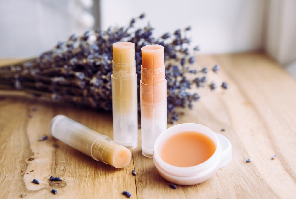 Make homemade natural organic ingredients lip balm. Handmade lip balm and lipstick inside container on natural wooden background and lavender for decoration.